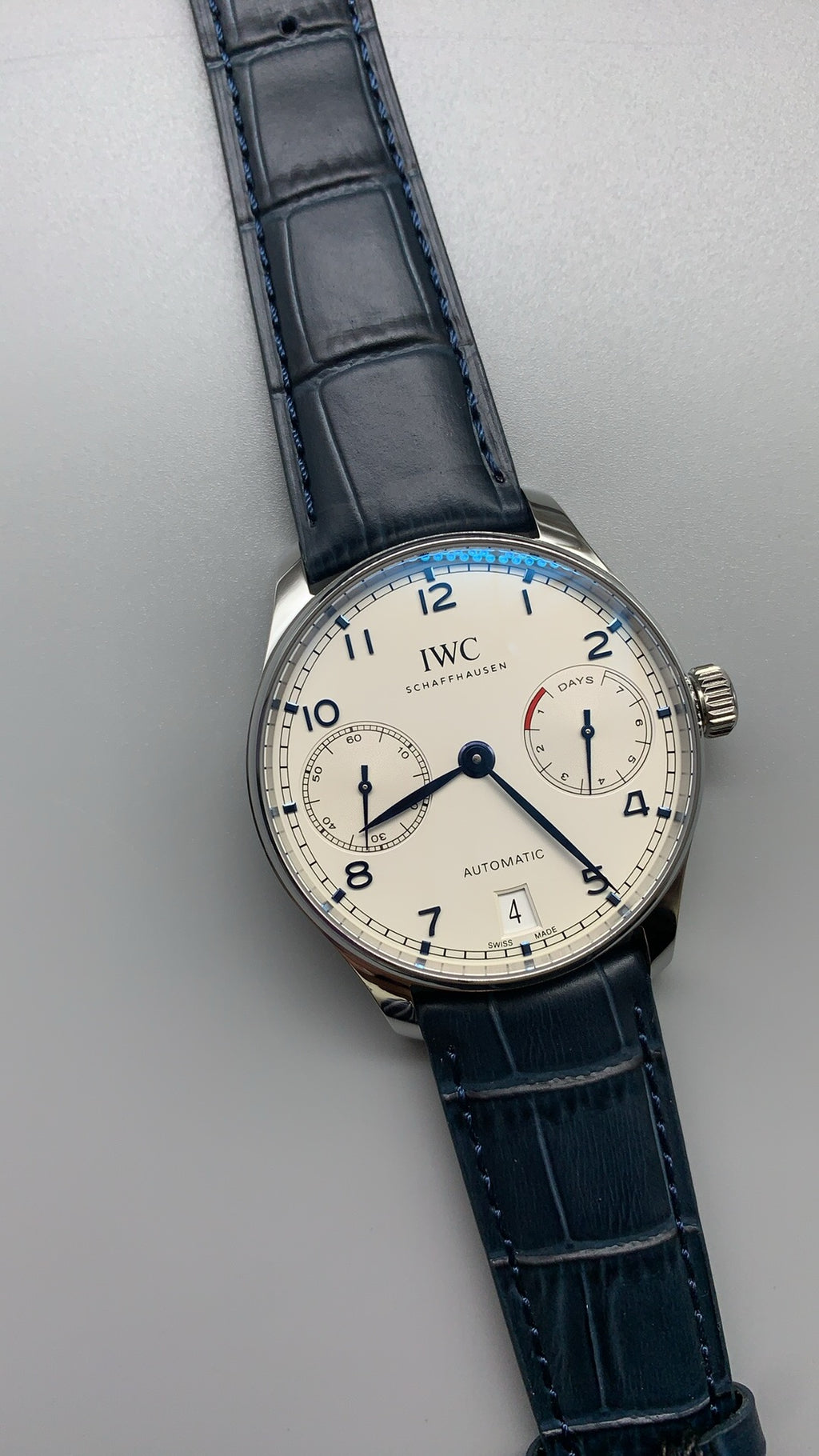 IWC Portugieser Automatic IW500705 | 42.3MM | ตัวเรือนสเตนเลสสตีล | หน้าปัดสีขาว | เข็มสีน้ำเงิน | สายหนังจระเข้สีน้ำเงิน | กลไกอัตโนมัติ Cal.52010